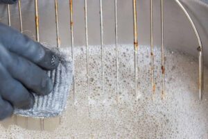 Person wearing rubber gloves cleaning grease off a metal grill in kitchen sink